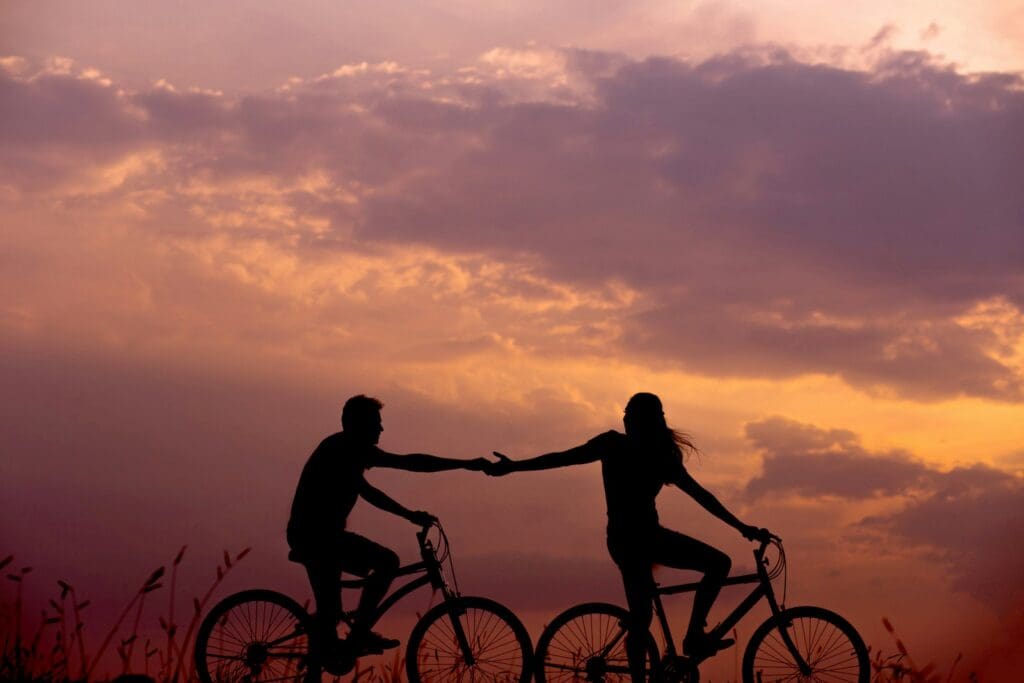 woman on bike reaching for man's hand behind her also on bike. When you're on a parenthood journey together, it's ok if one of you is a little further along at first