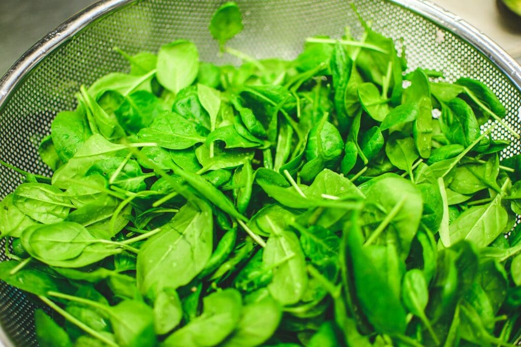 fresh leafy greens in a silver metal mixing bowl. Lots of these can improve your liver and hormone health.