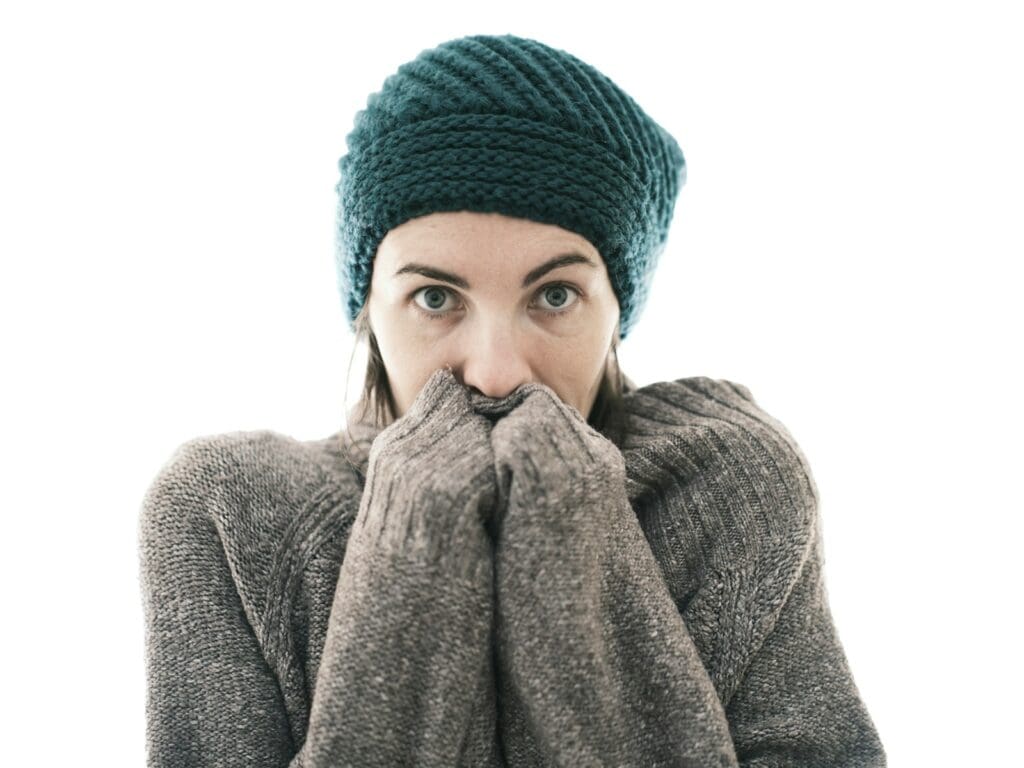 a woman covers her mouth with her hands wearing a sweater and hat. Feeling cold all the time can be a sign of thyrpid disorders in women