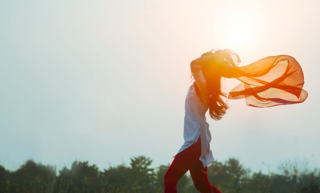 woman spreading s gauzy scarf during sunset, the sunlight filters through the material. she is in shadow 
