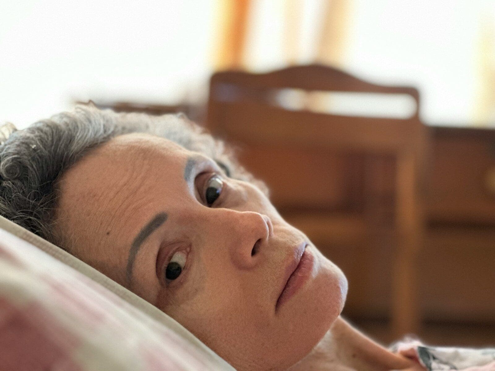 Photo by Gerardo González a white woman laying on a bed with her eyes open, she seems worried.