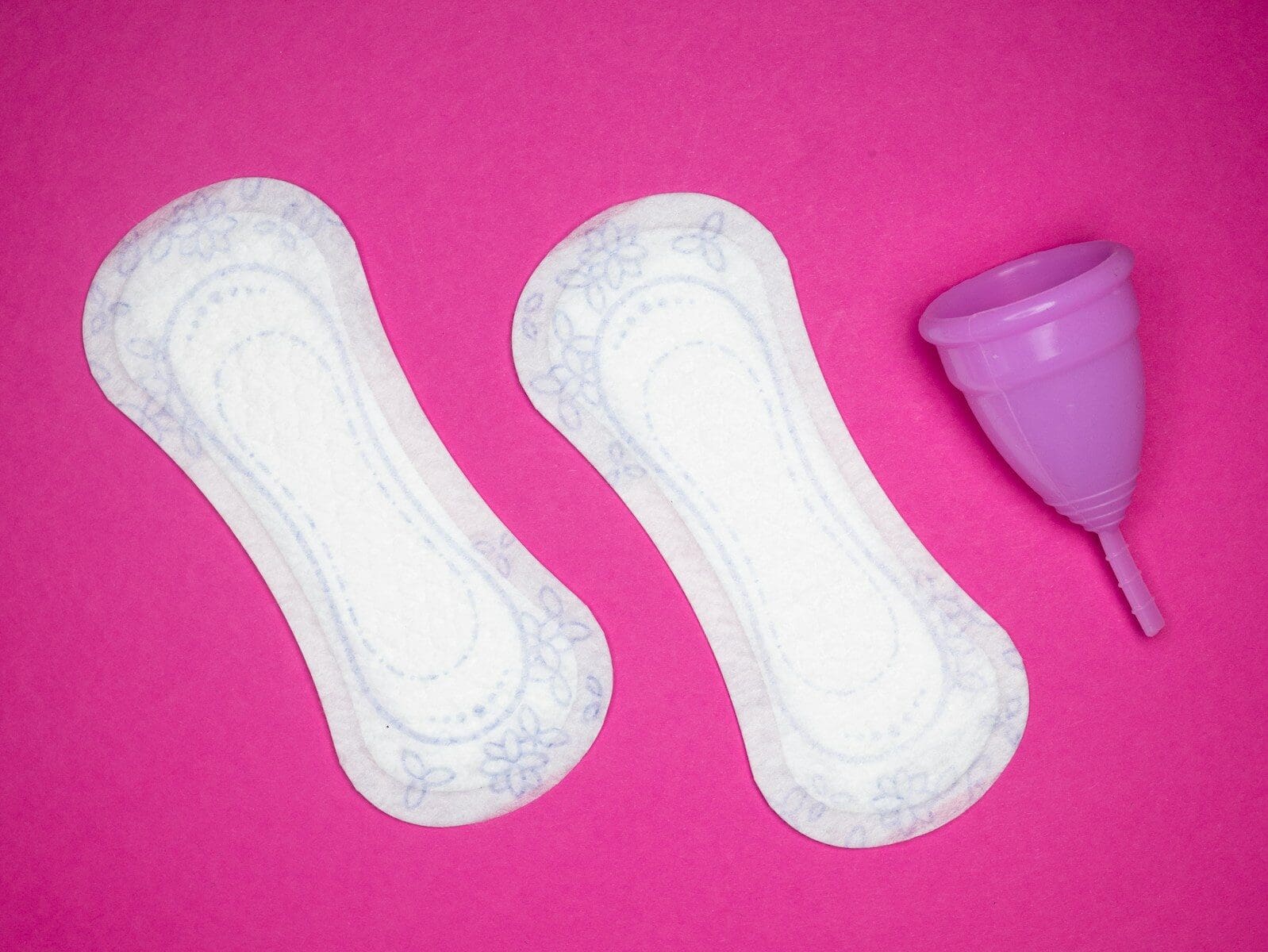 Photo by Reproductive Health Supplies Coalition a pair of menstrual pads next to a menstrual cup on a hot pink backgrouund. Naturopathic care for PMS can make your time of the month more bearable