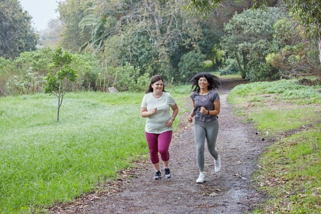 a couple of women running down a dirt road. Exercise with friends can be a great way to control PCOS symptoms. 