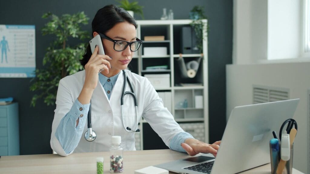 Female doctor on phone, working on laptop in office. Official PCOS diagnosis can be hard to come by