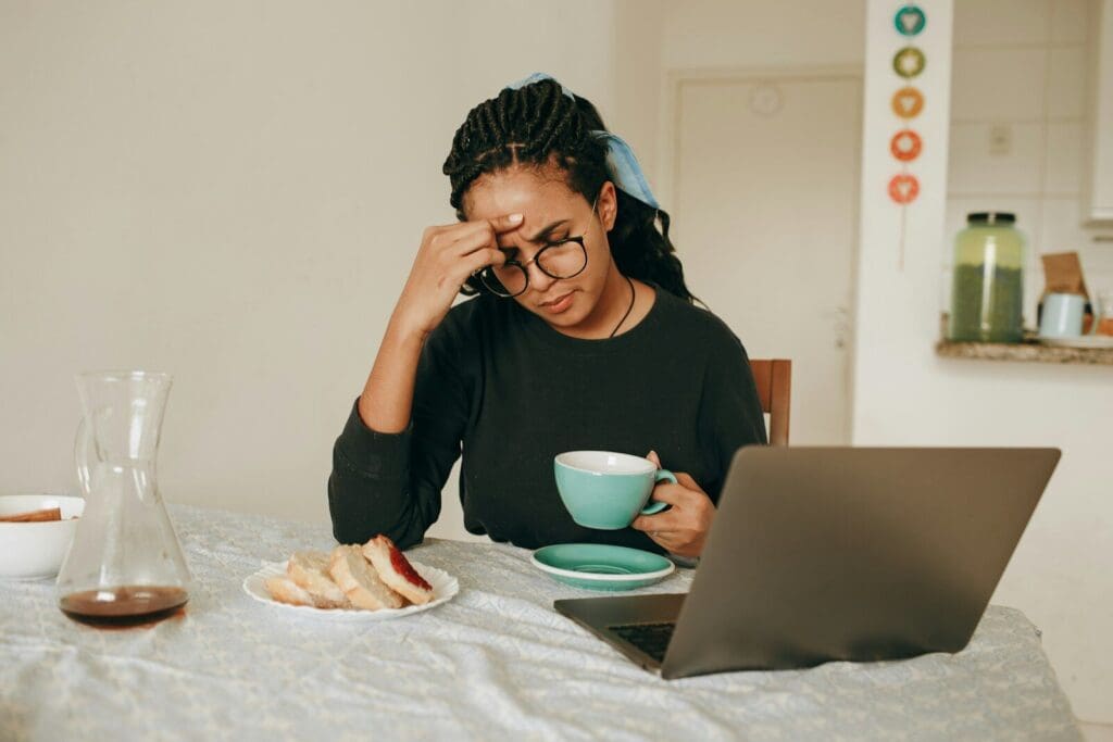 Black woman in black long sleeve shirt sitting and drinking coffee and looking at a laptop