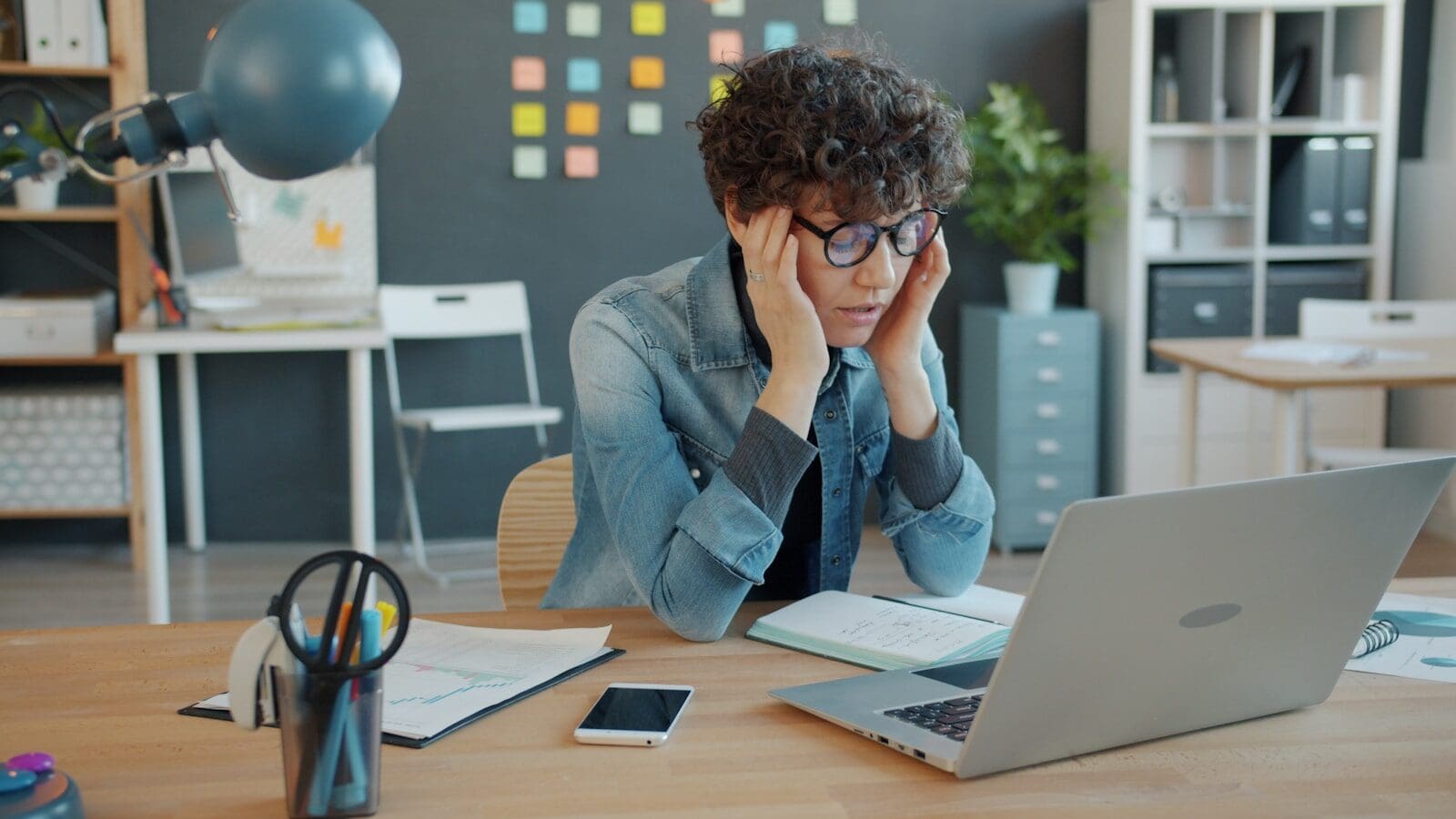 Photo by Vitaly Gariev A woman lwith glasses looking stressed at a laptop in an office. Is it work stress or a symptom of perimenopause?