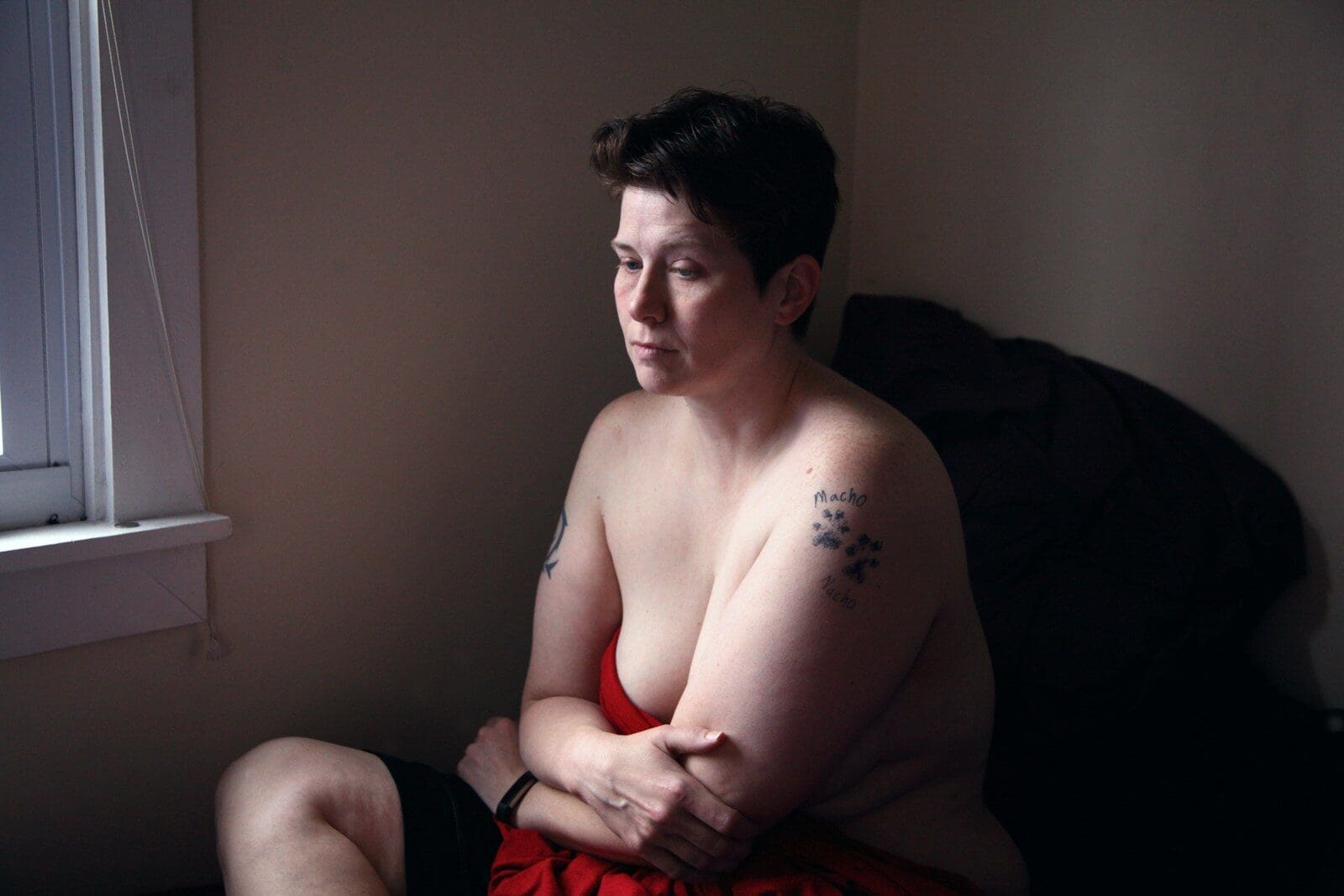 topless woman with shirt hair sitting on bed. PCOS symptoms can be brutal