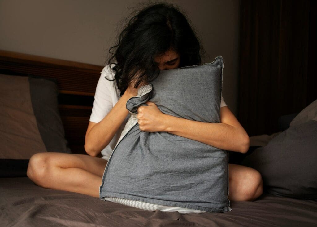 A woman sitting on a bed holding a pillow. Sleeplessness can be a sign of low testosterone.