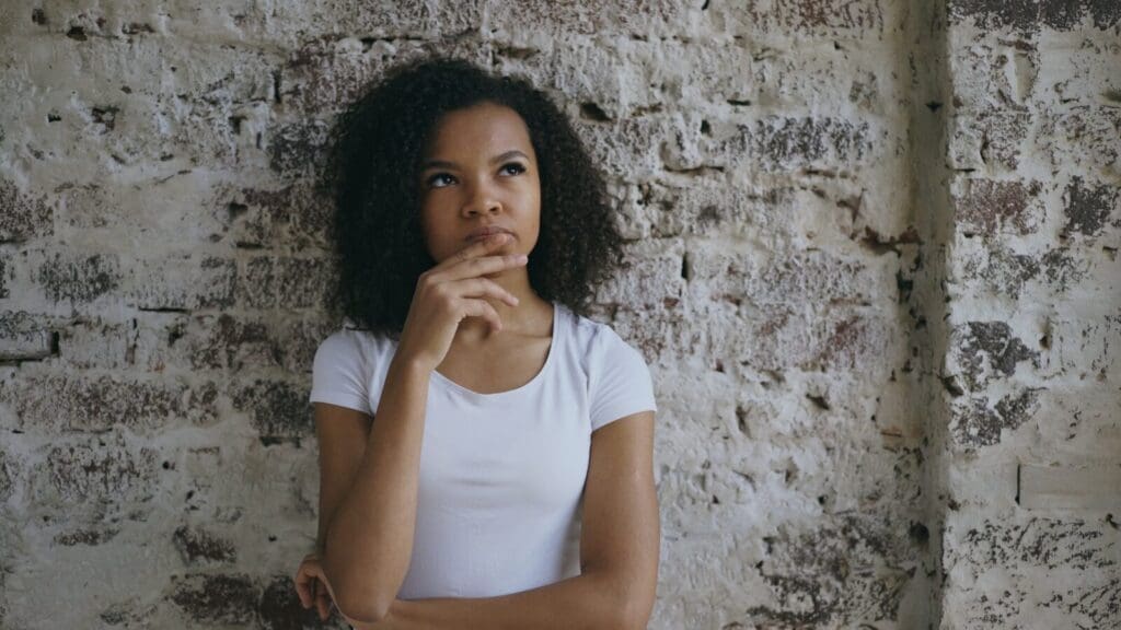 Young Black woman with hand on chin thinking. We all may be wondering if creatine is worth adding to our routine.